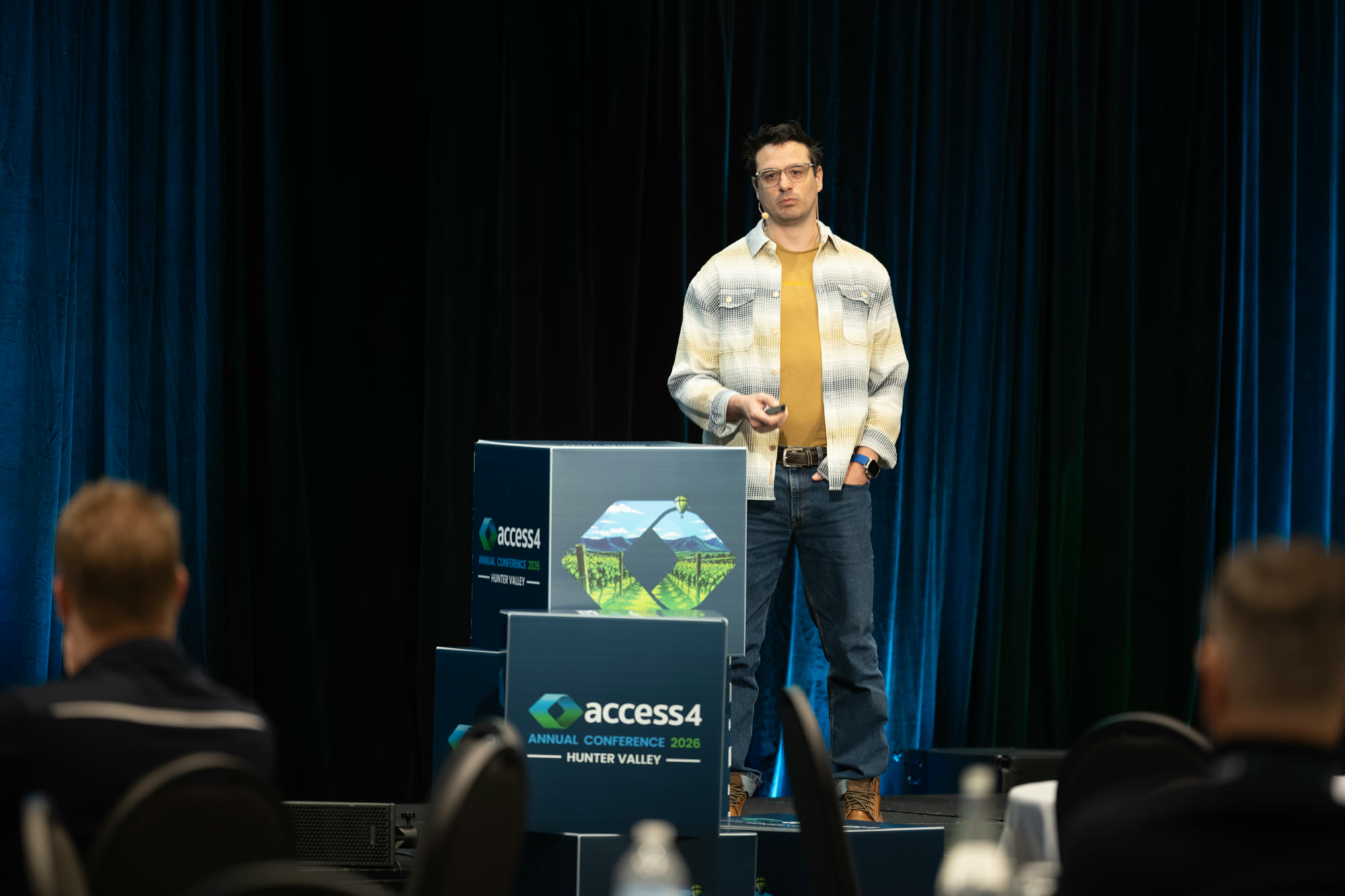 Diego Nievas standing on stage beside Access4 Annual Conference 2026 Hunter Valley banner stands, talking to the seated audience.